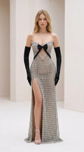 Front view of model wearing silver crystal strapless evening gown with black bow and high slit