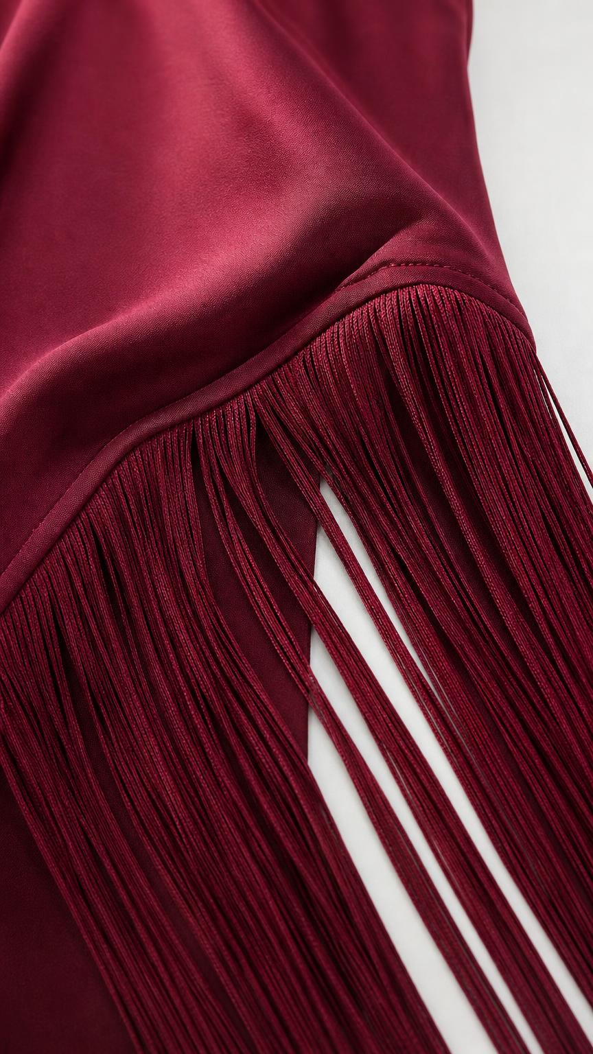 Close-up detail of smooth satin fabric and fringe hem in burgundy