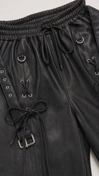 Close-up of black faux leather jogger pants with lace-up details and hardware
