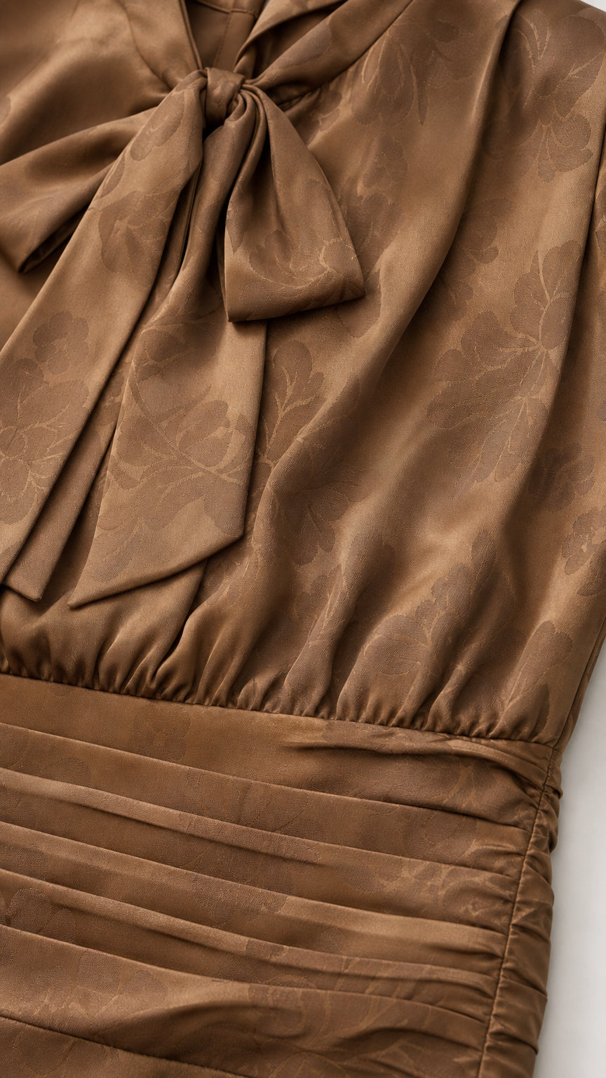 Close-up of the tie-neck bow and pleated waist detail on brown dress